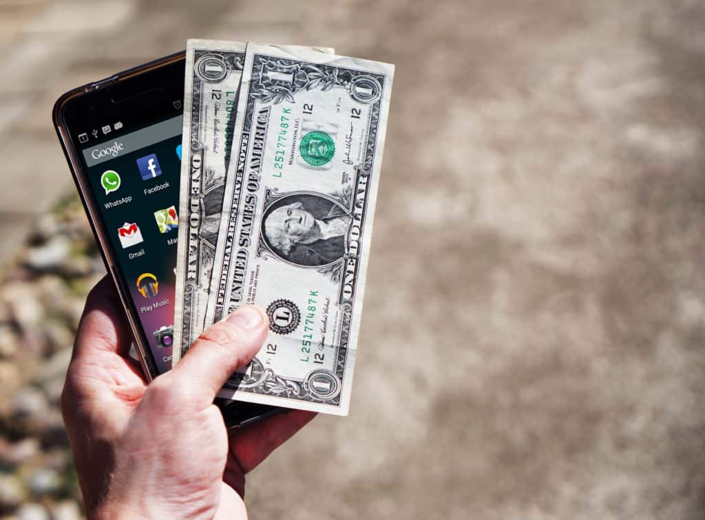 person holding smartphone and two $1 bills